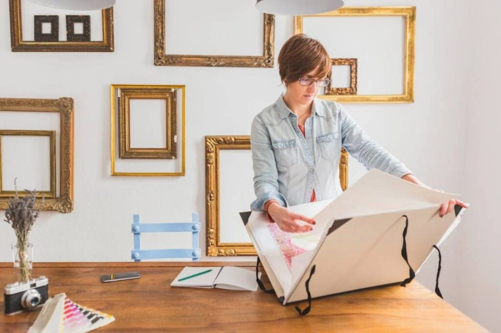 A woman examines artwork on a wooden table.