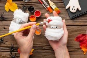 A person paints a small mummy figure wrapped in gauze.