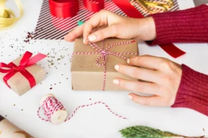 A person's hand ties red and white twine around a brown gift box.