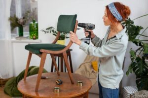 A person is assembling a green upholstered chair using a power drill.