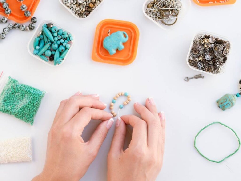 A person’s hands assemble colorful beads on a white surface.