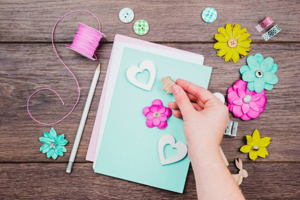 A hand placing a wooden decoration on a pastel-colored card.