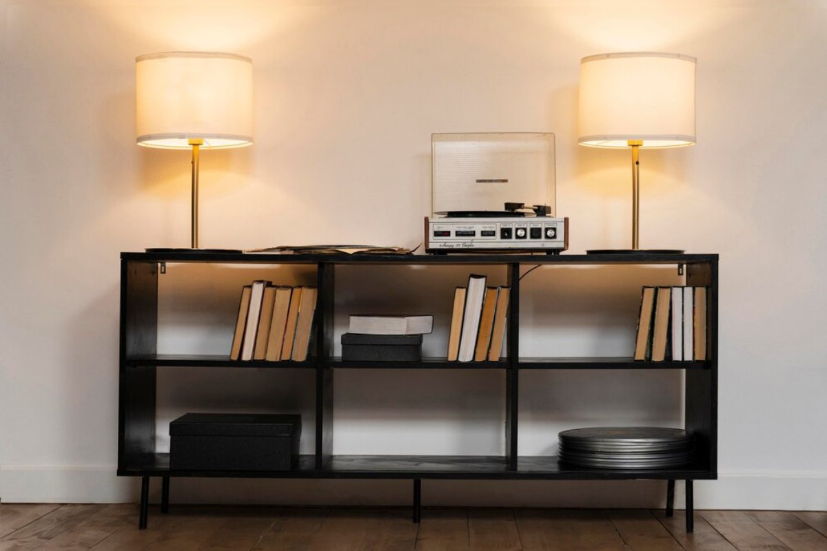 A black shelving unit displays books, a record player, and vinyl records, illuminated by two stylish lamps.