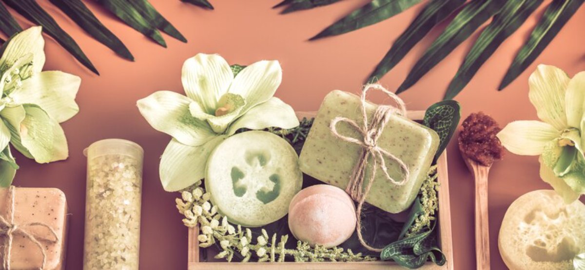 A spa arrangement featuring natural soaps, a bath bomb, cucumber slices, flowers, and decorative elements on a warm backdrop.