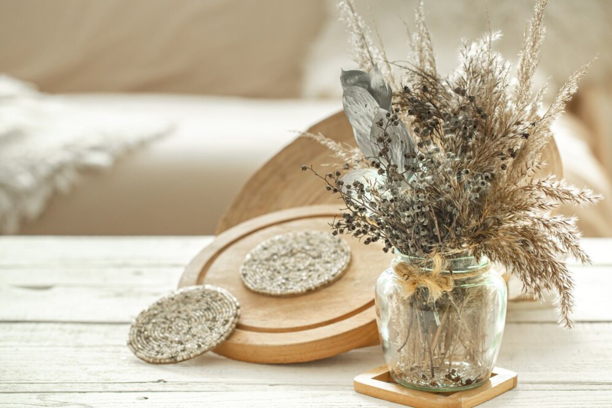 A rustic glass jar filled with dried flowers, paired with wooden coasters and a round cutting board, set on a light wooden surface.