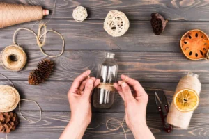 A person wraps twine around a glass bottle