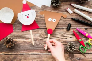 A hand holds a reindeer puppet beside a Santa puppet.