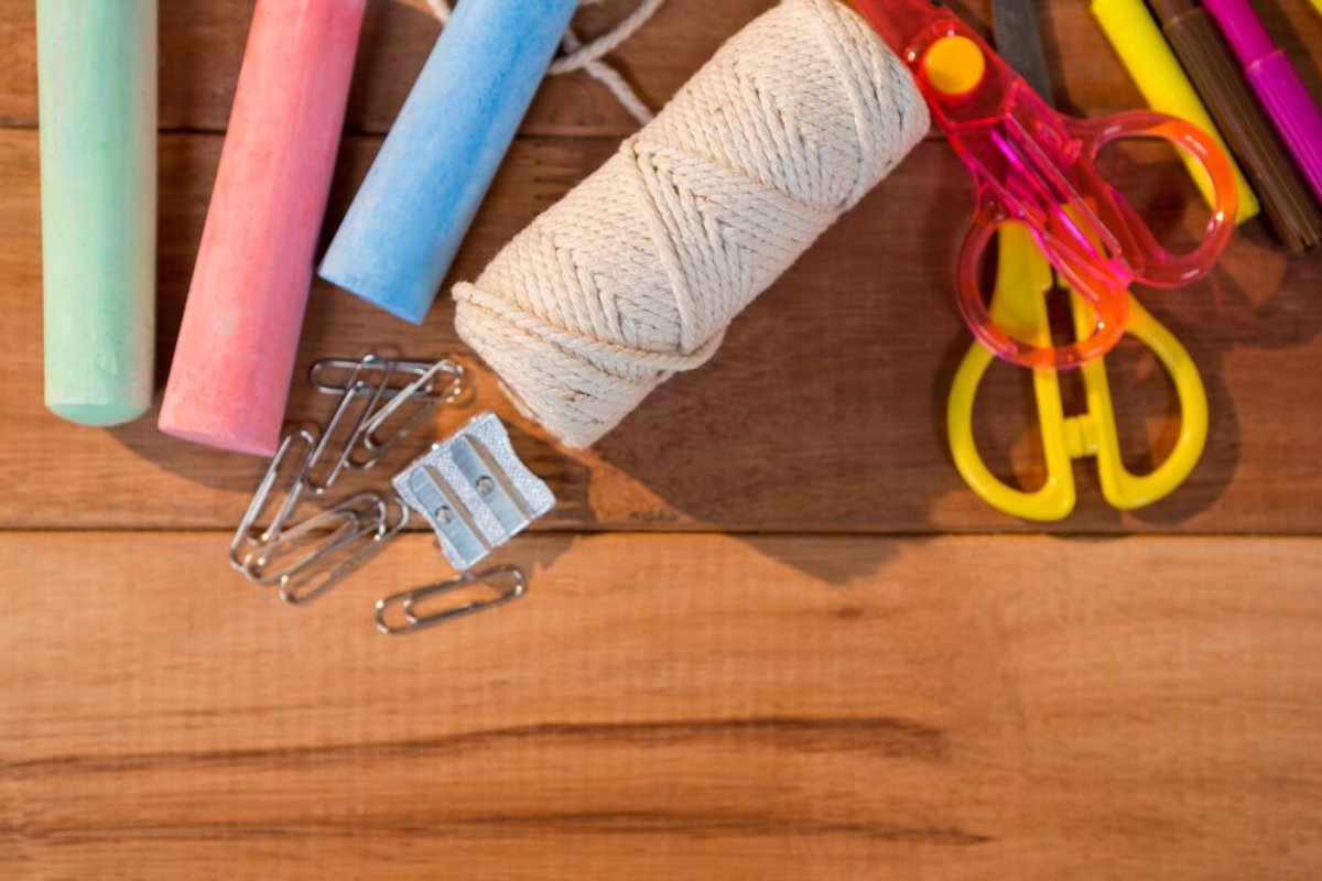 Colorful chalk sticks, scissors, paper clips, a sharpener, and twine on a wooden surface, suggesting a creative workspace.